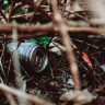 Close-up of a discarded can and trash in the underbrush, highlighting urban waste in nature.