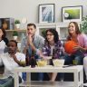 A group of young friends enthusiastically watching a sports event indoors with snacks and drinks.