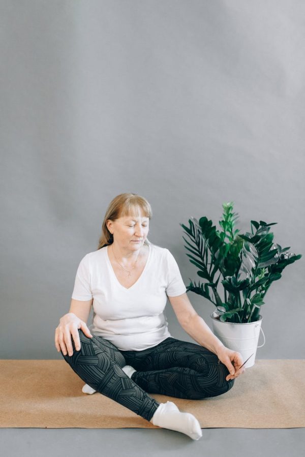 Elderly woman sits in yoga pose indoors, embracing mindfulness and relaxation.