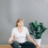 Elderly woman sits in yoga pose indoors, embracing mindfulness and relaxation.