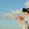 Woman using VR headset outdoors, exploring virtual reality under a clear blue sky.