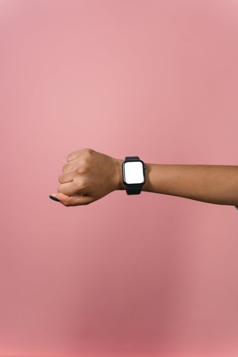 Hand displaying a smartwatch against a pink background, perfect for design mockups.