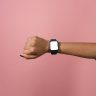 Hand displaying a smartwatch against a pink background, perfect for design mockups.