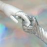 Close-up of a robot hand and silver-gloved hand touching, symbolizing human-robot connection.