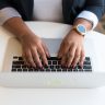 Woman's hands typing on a wireless laptop at a modern office desk, highlighting technology in business.