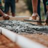 Construction workers leveling fresh cement on a sunny day at an outdoor site.