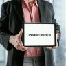 Professional holding a tablet with 'INVESTMENTS' text, ideal for finance and business themes.