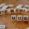 Close-up of wooden letter tiles on a table spelling 'News Musk', concept of media coverage.